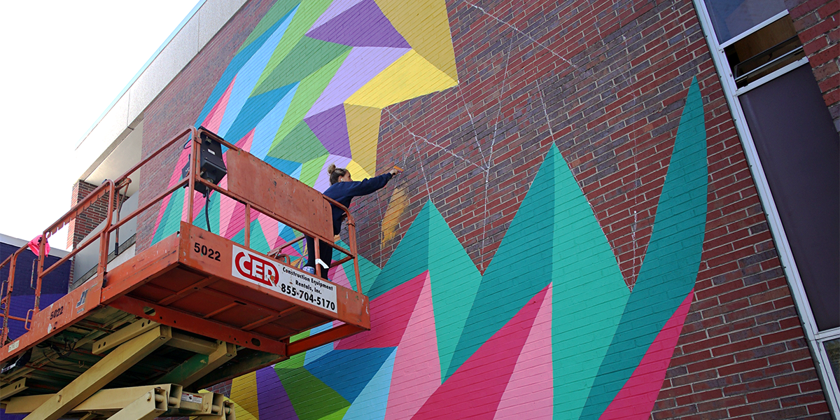 Photo of Kristin Farr painting a mural on the side of a brick building